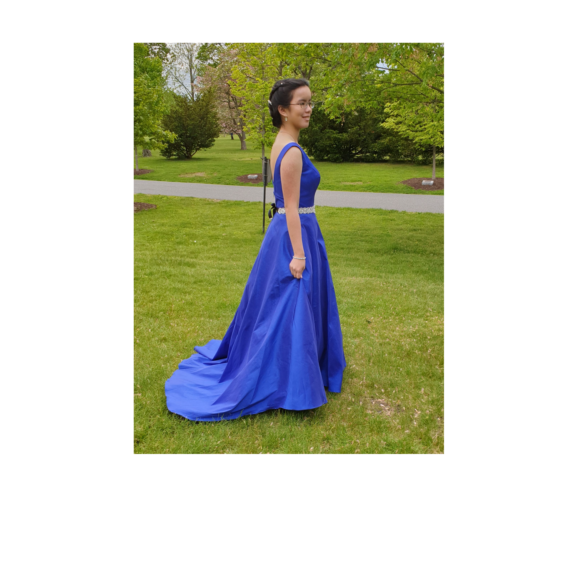 Liz is wearing a blue satin a line prom dress with a beaded sash and a low back. She is looking to the right.